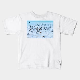 Flight of cormorant blurred in motion in flight over blue water Kids T-Shirt